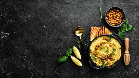 Photo for Hummus with chickpeas and rosemary in a black stone plate. Vegetarian food. Top view. On a black stone background. - Royalty Free Image