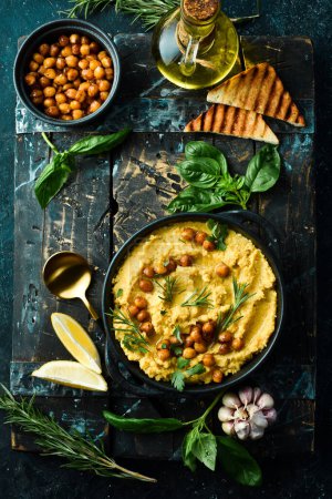 Téléchargez les photos : Hummus avec pois chiches et romarin dans une assiette en pierre noire. Nourriture végétarienne. Vue de dessus. Sur un fond de pierre noire. - en image libre de droit