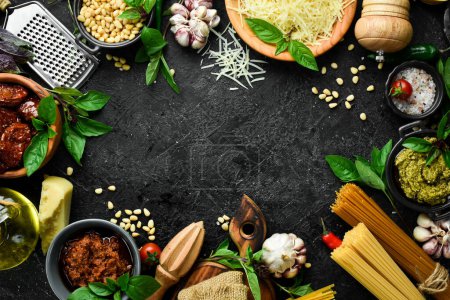 Photo for Cooking background: pasta, basil, parmesan, pesto, tomatoes and nuts, olive oil. On a black stone background background. - Royalty Free Image