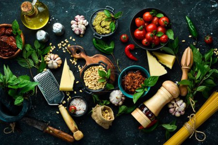 Photo for Cooking background: pasta, basil, parmesan, pesto, tomatoes and nuts, olive oil. On a black stone background background. - Royalty Free Image