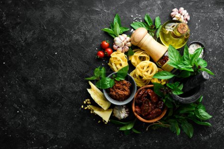 Téléchargez les photos : Cuisine italienne : pâtes, basilic, parmesan, pesto, tomates et noix, huile d'olive. Sur un fond de pierre noire. - en image libre de droit