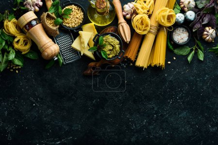 Photo for Preparation of pasta with pesto sauce and sun-dried tomatoes. Italian traditional cuisine. On a black stone background background. - Royalty Free Image