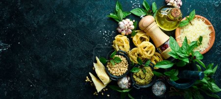 Photo for Preparation of pasta with pesto sauce and sun-dried tomatoes. Italian traditional cuisine. On a black stone background background. - Royalty Free Image