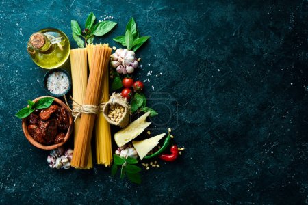 Photo for Cooking spaghetti with pesto sauce and sun-dried tomatoes. Ingredients: Spaghetti, basil, parmesan, pine nuts, tomatoes, spices. Italian traditional cuisine. On a concrete background. - Royalty Free Image