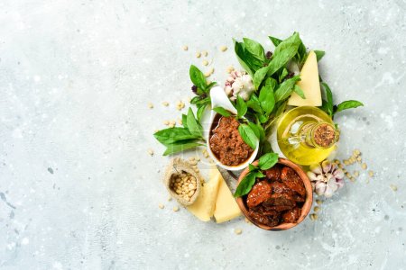 Photo for Preparation of traditional Italian pesto sauce with dried tomatoes. Ingredients: basil, parmesan, pine nuts, tomatoes, spices. On a concrete background. - Royalty Free Image