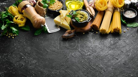 Téléchargez les photos : Sauce pesto traditionnelle. Ingrédients : Basilic, pignons, parmesan et huile d'olive. Sur un fond de pierre noire. - en image libre de droit