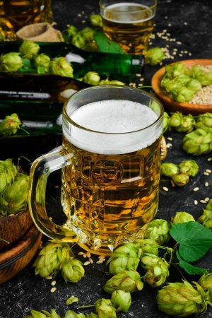 Foto de Cerveza fresca en vasos y lúpulo verde fresco sobre un fondo de piedra negra. Banner. - Imagen libre de derechos