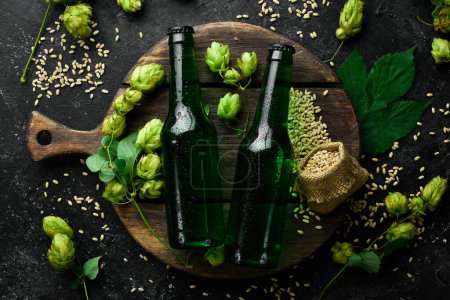 Foto de Lúpulo fresco, vasos y cerveza. Cerveza ligera en botellas de vidrio sobre un fondo de piedra negra. Banner de cerveza. - Imagen libre de derechos