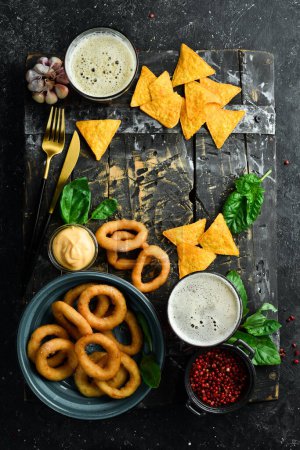 Photo for Two glasses of beer and salty beer snacks on a wooden tray. On a black stone background. - Royalty Free Image