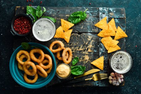 Photo for Two glasses of beer and salty beer snacks on a wooden tray. On a black stone background. - Royalty Free Image
