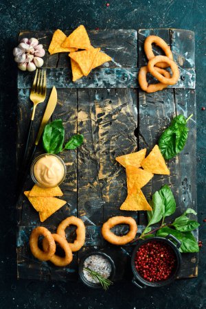 Foto de Snacks salados para cerveza: aros de cebolla a la parrilla y nachos. Sobre un fondo de piedra negra. - Imagen libre de derechos