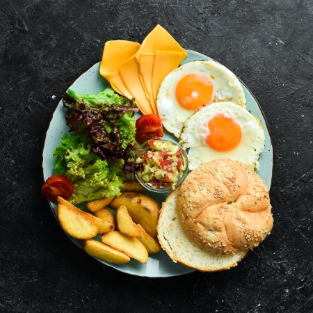 Foto de El desayuno. Huevos revueltos, bollo, queso, ensalada y salsa. Sobre un fondo de piedra negra. - Imagen libre de derechos