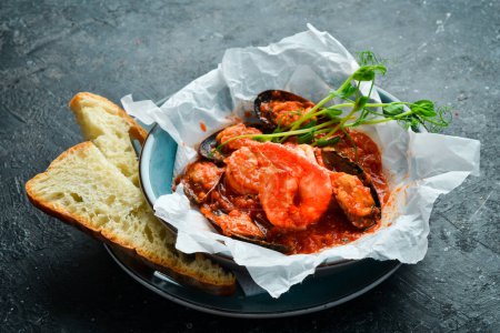 Téléchargez les photos : Fruits de mer. Crevettes et moules cuites dans une sauce tomate, servies avec des croûtons. Sur un fond de pierre noire. - en image libre de droit