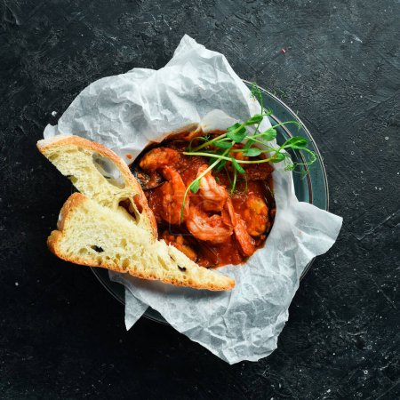 Photo for Seafood. Shrimps and mussels cooked in tomato sauce, served with croutons. On a black stone background. - Royalty Free Image