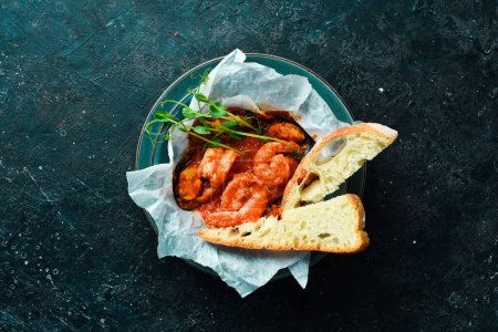 Téléchargez les photos : Fruits de mer. Crevettes et moules cuites dans une sauce tomate, servies avec des croûtons. Sur un fond de pierre noire. - en image libre de droit