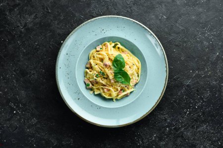 Foto de Pasta carbonara con tocino, queso y albahaca en un plato. Plato italiano. Sobre un fondo de piedra negra. - Imagen libre de derechos