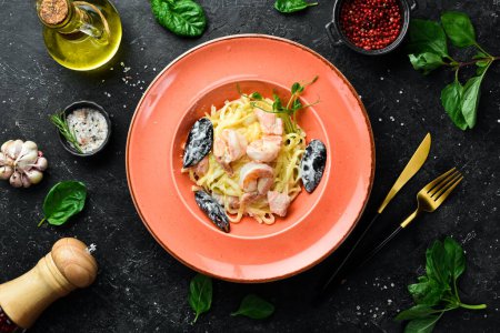 Téléchargez les photos : Fruits de mer. Pâtes avec crevettes, moules, fromage et basilic dans une assiette. Un plat italien. Sur un fond de pierre noire. - en image libre de droit