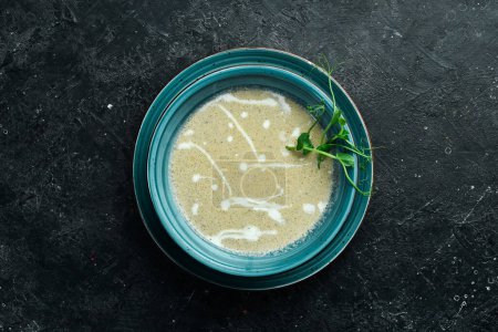 Foto de Sopa de crema de champiñones con crema y conjuto. En un plato azul. Sobre un fondo de piedra negra. - Imagen libre de derechos