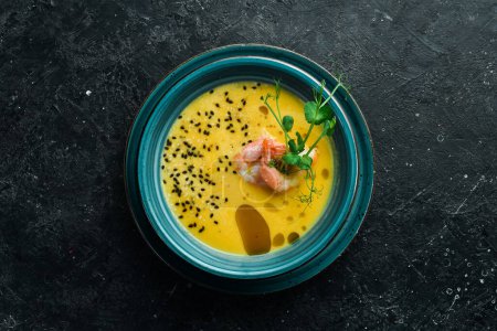 Photo for Autumn menu. Pumpkin soup with shrimp, olive oil and sesame seeds. In a blue bowl. On a black stone background. - Royalty Free Image