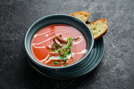 Téléchargez les photos : Soupe de tomates avec bacon, oignon et crème. Cuisine mexicaine. Sur un fond de pierre noire. - en image libre de droit