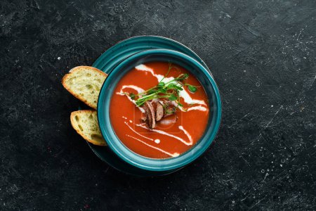 Téléchargez les photos : Soupe de tomates avec bacon, oignon et crème. Cuisine mexicaine. Sur un fond de pierre noire. - en image libre de droit