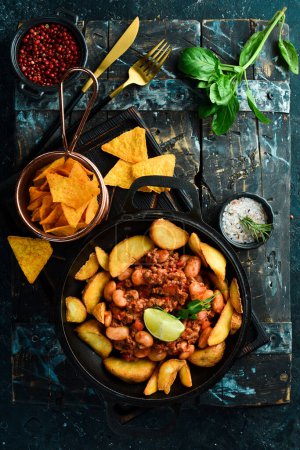 Photo for Fried potatoes with beans and meat in a pan. On a black stone background. - Royalty Free Image