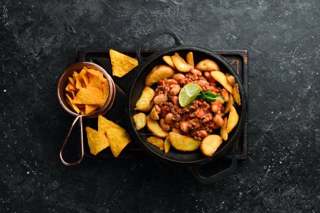 Photo for Fried potatoes with beans and meat in a pan. On a black stone background. - Royalty Free Image