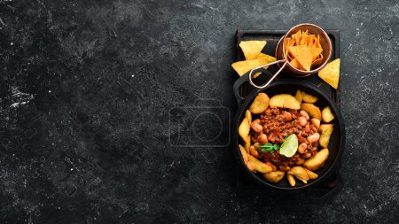 Téléchargez les photos : Pommes de terre frites avec haricots et viande dans une casserole. Sur un fond de pierre noire. - en image libre de droit