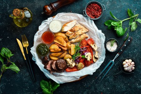 Photo for Barbecue. Grilled veal steak and chicken breast with grilled vegetables on a wooden board. On a black stone background. - Royalty Free Image