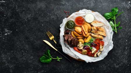 Photo for Barbecue. Grilled veal steak and chicken breast with grilled vegetables on a wooden board. On a black stone background. - Royalty Free Image