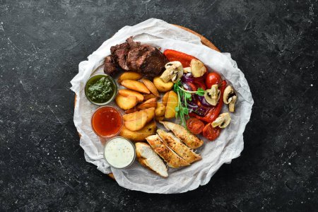 Téléchargez les photos : Barbecue. Steak de veau grillé et poitrine de poulet avec légumes grillés sur une planche en bois. Sur un fond de pierre noire. - en image libre de droit