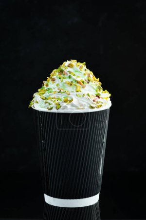 Photo for Coffee with pistachios and cream in a paper cup. on a black background. Free space for text. - Royalty Free Image