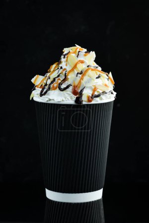 Foto de Café con caramelo y crema en una taza de papel. sobre un fondo negro. Espacio libre para texto. - Imagen libre de derechos