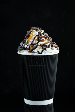 Foto de Café con caramelo y crema en una taza de papel. sobre un fondo negro. Espacio libre para texto. - Imagen libre de derechos