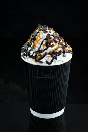 Coffee with caramel and cream in a paper cup. on a black background. Free space for text.