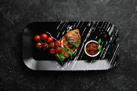 Photo for Baked chicken fillet with basil and salsa sauce on a black plate. Top view. Free space for text. - Royalty Free Image