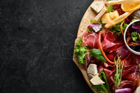 Photo for Antipasto Assortment of appetizers: cheese, prosciutto, salami, bacon, olives and capers on a wooden board. Top view. Free space for text. - Royalty Free Image