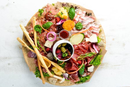 Photo for Antipasto Assortment of appetizers: cheese, prosciutto, salami, bacon, olives and capers on a wooden board. Top view. Free space for text. - Royalty Free Image