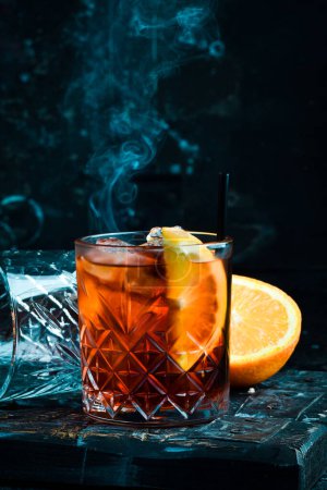 Téléchargez les photos : Cocktail classique Negroni dans un verre rétro avec glace et écorce d'orange sur fond noir. Menu bar. - en image libre de droit