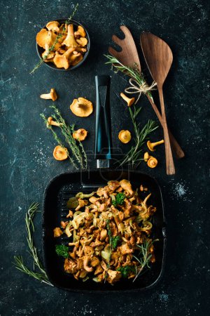 Téléchargez les photos : Champignons Chanterelle frits avec des oignons et des épices dans une casserole sur la table de cuisine. Vue de dessus. Espace libre pour le texte. - en image libre de droit