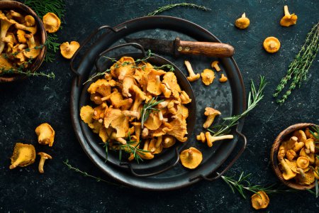 Photo for Organic wild chanterelle mushrooms in a bowl. On a black stone background. Top view. - Royalty Free Image