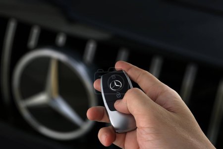 Photo for Right hand holding car remote key of Benz c200 coupe AMG dynamic model with background of Mercedes Benz chromium grille with Benz star logo park in the dark garage - Royalty Free Image