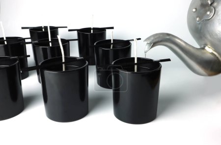 Photo pour Many luxury black glasses on white table are used as containers for making of aroma scented candle poured with natural organic soy wax before selling in the home fragrance products - image libre de droit