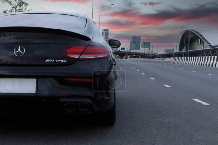 Photo for Nice design led tail light or tail lamp and rear wing spoiler of black sports car brand Mercedes Benz c200 AMG coupe model park on the road near train station with background of beautiful twilight sky - Royalty Free Image