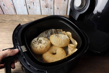 homemade organic butter bagel breads are baked by using a black air fryer or oil free fryer appliance for being breakfast in the morning before going to work with background of wooden table and wall