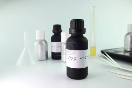 Téléchargez les photos : Bouteille d'huile essentielle noire est sur la table blanche avec du papier buvard, bouteille de parfum et échelle numérique sont utilisés pour mélanger le parfum agréable pour la fabrication de parfum et de bougie par le parfumeur en laboratoire - en image libre de droit
