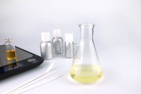 Foto de Chemical beaker , flask is on white table with blotting paper , fragrance bottle and essential oil bottle are used to blend the nice scent for making perfume and candle by perfumer in the laboratory - Imagen libre de derechos