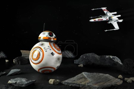 Téléchargez les photos : Un personnage de robot droïde dans le film Star Wars nom BB-8 (ou Beebee-Ate) affichage sur la table de pierre avec fond de X-wing Starfighter dans l'espace noir de nombreuses étoiles mur dans la boutique de jouets de film de guerre étoile - en image libre de droit