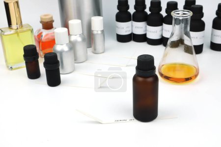 amber color essential oil bottle is on white table with blotting paper , fragrance bottle and digital scale are used to blend the nice scent for making perfume and candle by perfumer in laboratory