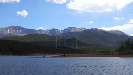 Fishing on Crystal Creek Reservoir Colorado features water in the foreground and mountains and sky in the background with people fishing in the middle ground near Pikes Peak in Colorado
